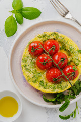 Frittata with arugula, potatoes and cherry tomatoes in iron pan on old stone table background. Top view.