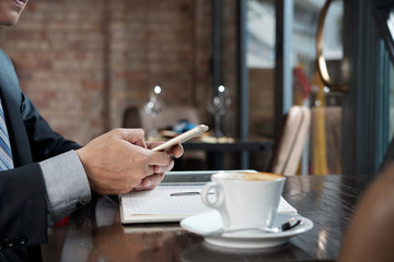Cup of cappuccino and hands of businessman texting colleagues