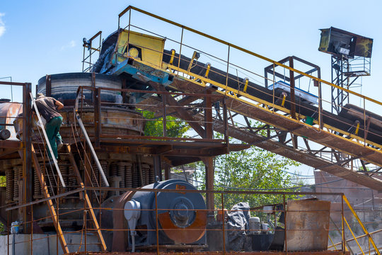 Crushing machinery, cone type rock crusher, conveying crushed granite gravel stone in a quarry open pit mining. Processing plant for crushed stone and gravel. Mining and Quarry mining equipment.