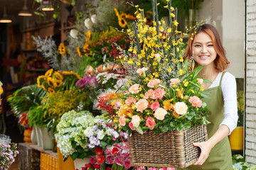 Portrait of cheerful young florist with basket of beautiful flowers smiling at camera