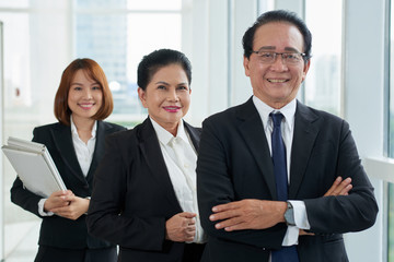 Portrait of successful Asian business team of three standing in modern office