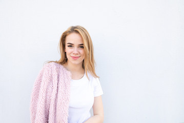 Attractive lady in a white T-shirt and pink coat, smiles and looks at the camera on a white background. Copyspace