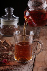 A stream of rooibos tea pouring from the teapot to a transparent glass cup