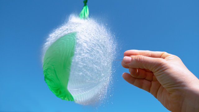 CLOSE UP: Unrecognizable person holding a needle pierces a green water balloon.