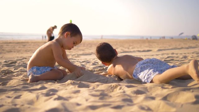 Slow motion 4K - Two little brothers playing and smiling in the beach in a sunny day