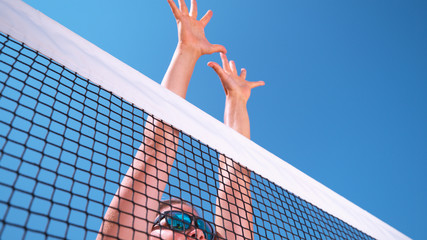 LOW ANGLE: Young female beach volleyball player jumps up to block the ball.