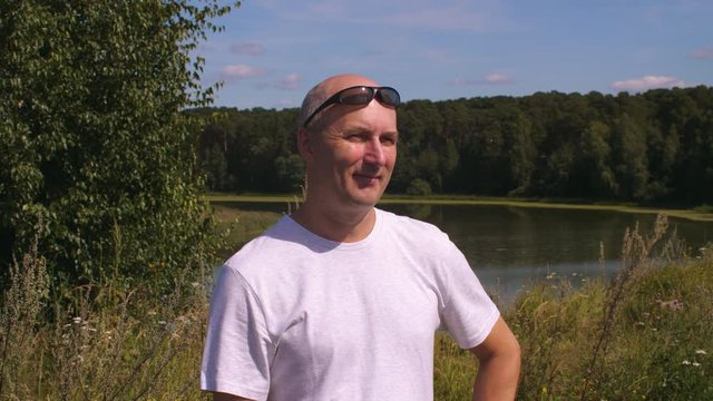 Cheerful adult man looking on green forest with lake and enjoying summer day