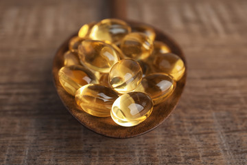 Spoon with cod liver oil pills on table, closeup