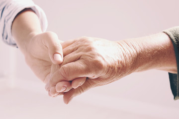 Woman holding hands with senior lady on light background, closeup. Elderly care and help concept
