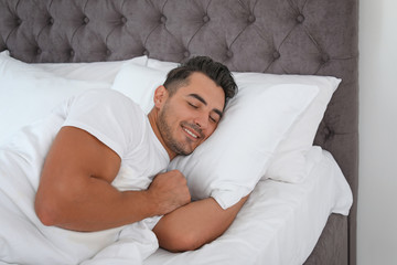 Young man sleeping in bed with soft pillows at home