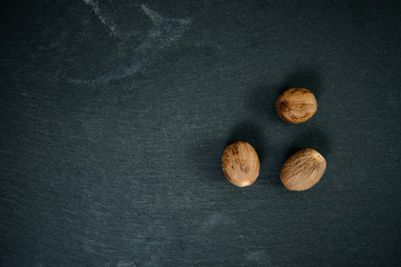 A spice nutmeg on a wooden bucket. Food photography of nutmeg seeds on a dark, black stone. Top view of scattered nutmeg seeds. The concept of seasoning food.