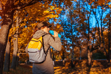 Obraz na płótnie Canvas Tourist with backpack walking in autumn forest. Young woman drinking water