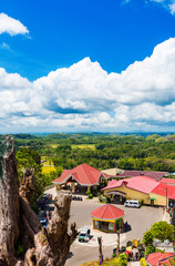 View of buildings on the background of the Chocolate hills on sunny day on Bohol island, Philippines. Vertical.