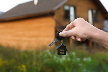 Real estate agent holding key and blurred house on background. Focus on hand