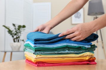 Woman folding bright clothes on table indoors. Rainbow colors