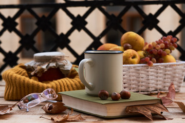 Cup of coffee old book glasses and autumn leaves with fruit basket on rustic wooden table on terrace background. Morning breakfast, seasonal, book reading, Sunday relaxing and still life concept