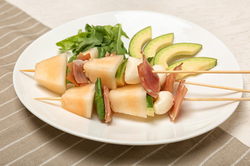 Plate with melon, mozzarella and prosciutto skewers on table