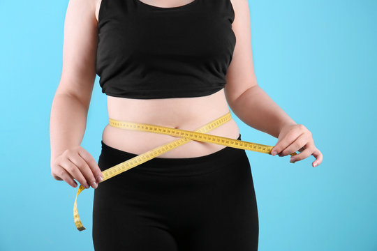 Overweight woman measuring waist before weight loss on color background