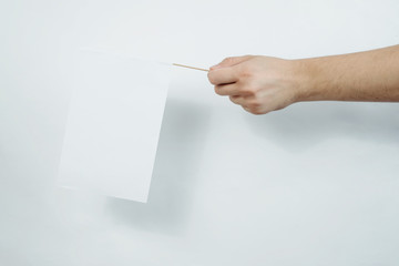 Hand holding a white, blank flag. Content completion concept. Blank white flag side view. Flag on a light, white background.