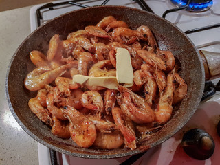Giant orange shrimps with heads fried in oil in a frying pan on a gas stove
