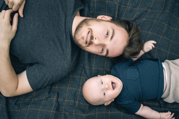 Happy father and his baby son top view. Family portrait from above with 5-months child lying in park. Looking at camera, smiling, having fun.  Father's Day concept