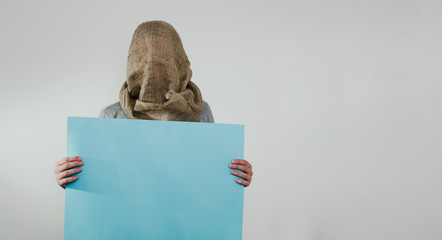 A man with a veiled face on a light background with a blue blank signboard. The concept of...