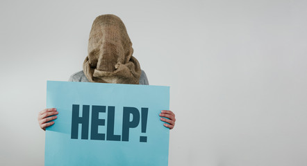 Man with veiled face on a light background with a blue board with the word HELP. The concept of kidnapping, detention, and crime. No face. The man has a bag on his head. Kidnapping by terrorists.