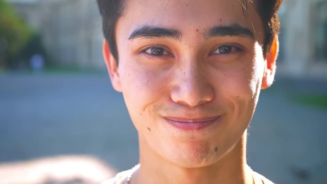 Beautiful asian happy boy is laughing in braces and looking aside, while standing on the street