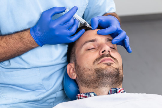 Close up of beautician expert's hands injecting botox in man's forehead.