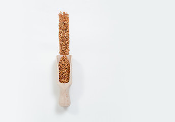 Dried mustard seeds. Yellow charlock scattered on a white background and a wooden scoop. The concept of using herbs and spices for dishes. Strong taste of dishes. Improving the taste.