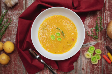 Overhead view of warm bowl of vegetarian soup with ingredients on rustic red barn wood background