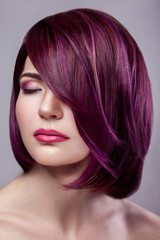 Portrait of beautiful fashion model woman with short purple colored hairstyle and makeup with calm closed eyes. indoor studio shot, isolated on gray background.