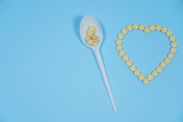 Pills - medicines are poured in the form of heart on a blue background and spoon.