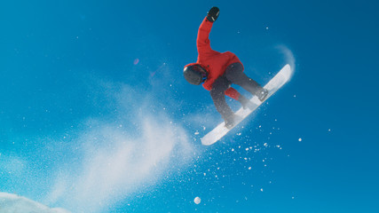 Athletic man in red winter jacket snowboarding and doing tricks in the air.