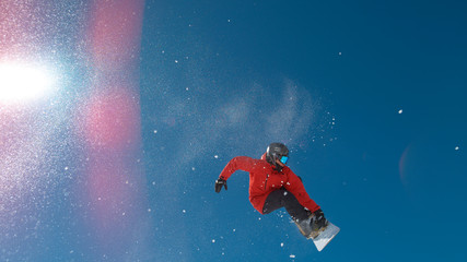 LENS FLARE: Bright winter sun shines on snowboarder doing a spinning grab trick.