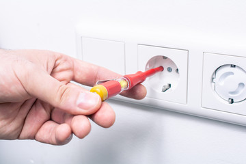 The Hand Of An Electrician Holding A Phase Tester In A Wall Socket, The Glowing Light Indicates An Active Current
