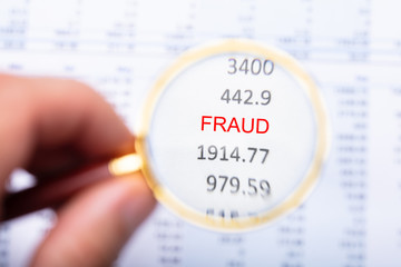 Man Examining Fraud Word On Financial Report