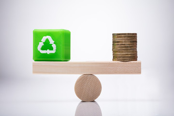 Cubic Block With Recycle Symbol And Coins Balancing On Seesaw