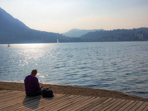 man reads book in a park sitting on the shore of the lake in Lugano, Switzerland