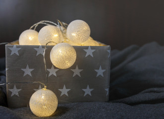 White cotton ball light garland in a grey basket wit stars sparkling at home. close up, bright lights, festive atmosphere. home decoration. New year and Christmas celebration concept