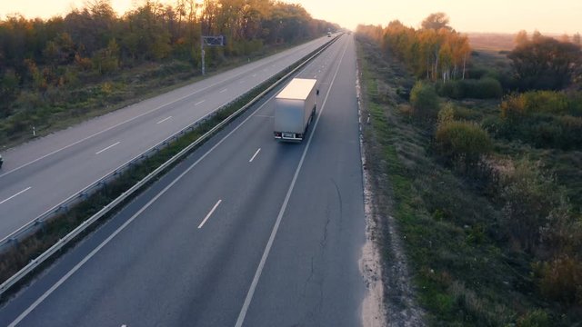 Aerial view of white semi truck with cargo trailer moving on the highway at sunset