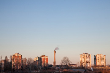 Communist housing buildings facing a polluting chimney smoking & an abandoned factory in Pancevo, Serbia. The towers are a symbol of Socialist architecture and  economic transition of Eastern Europe