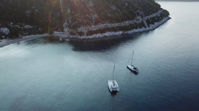 Aerial orbital view of a greek bay with green and bule sea with Sailboats anchored,Early morning sunlight