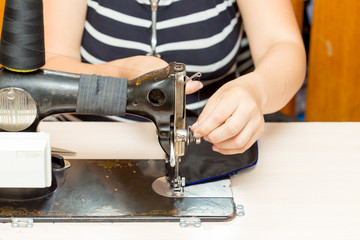 Pretty female tailor sits at table with sewing machine and sews fabric.