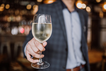 A young man holding a glass of white wine. Restaurant, catering, hospitality and beverage concept.