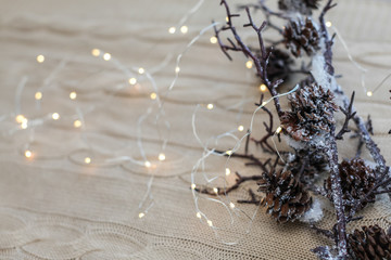 Christmas and New Year composition. Close up snow branches with cones and garland on knitted white background.