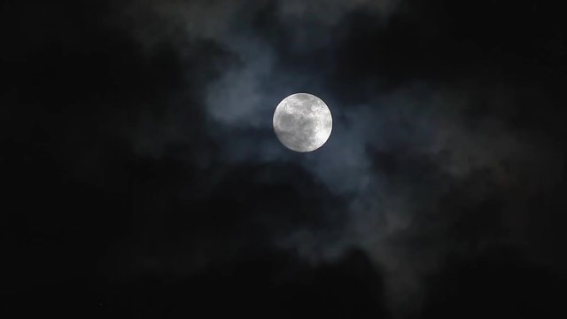 Black clouds passing in front of the moon in the night sky. Outdoor at nighttime..