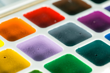 Abstract of new unused palette of children's multicolor watercolor paints with paint brush. Extreme shallow DOF with some blur in foreground.