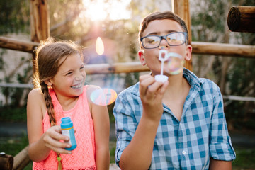 Fototapeta premium Young boy and girl having fun blowing soap bubbles