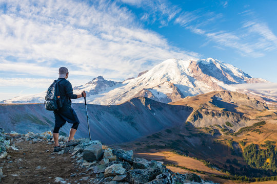 A hiker looking at Mount Rainier with hiking poles in his hand
